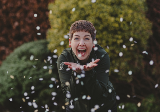 Woman with short hair, smiling and blowing confetti in a garden